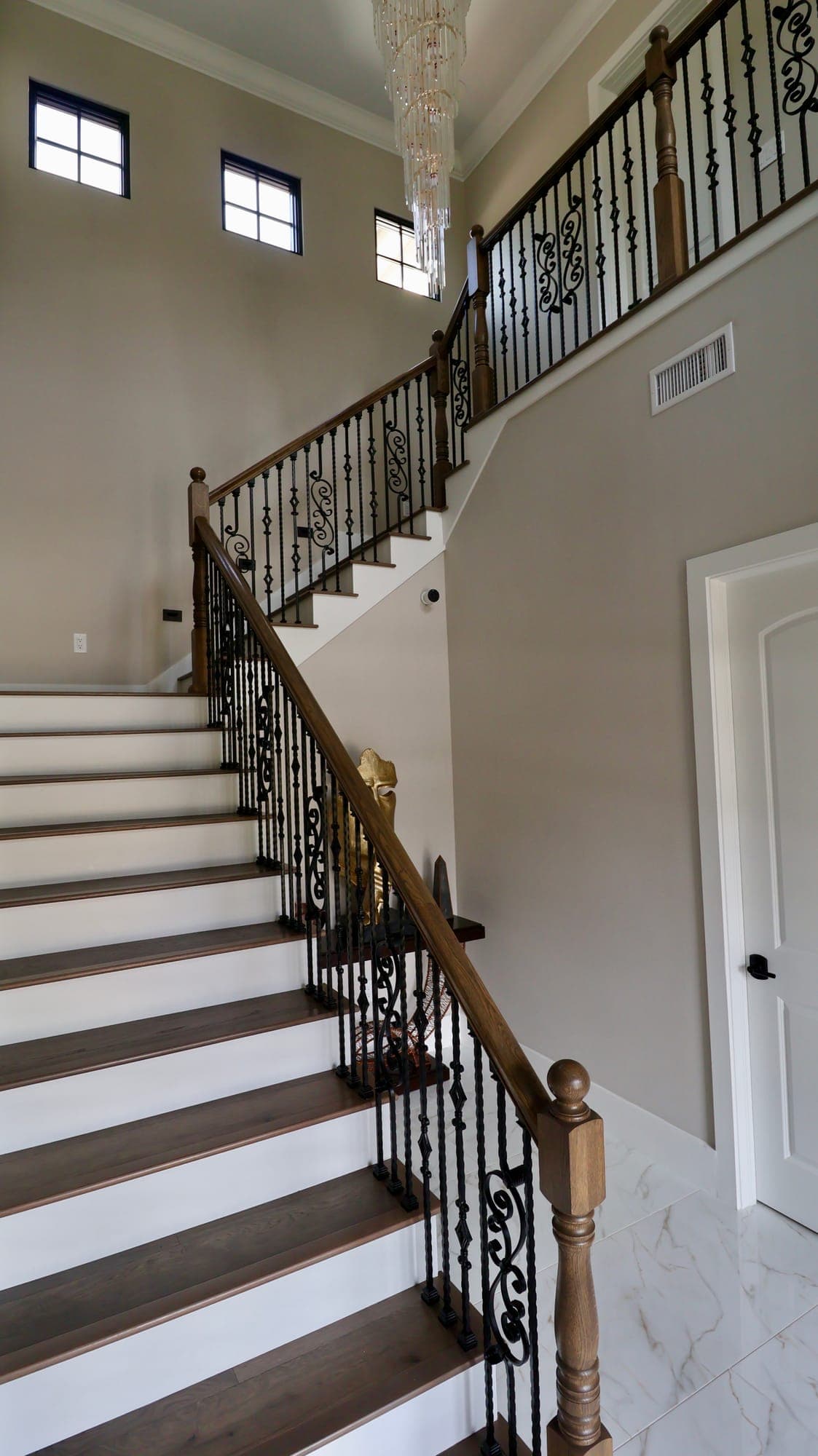 Custom staircase with stained wood treads, hand-forged iron scroll balusters, and a wood handrail in a custom home in Nocatee, Florida