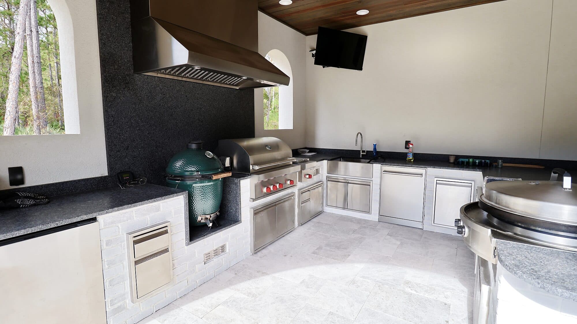 Covered outdoor kitchen with a built-in grill, ceramic smoker, and stone counters at a custom home in Nocatee, Florida
