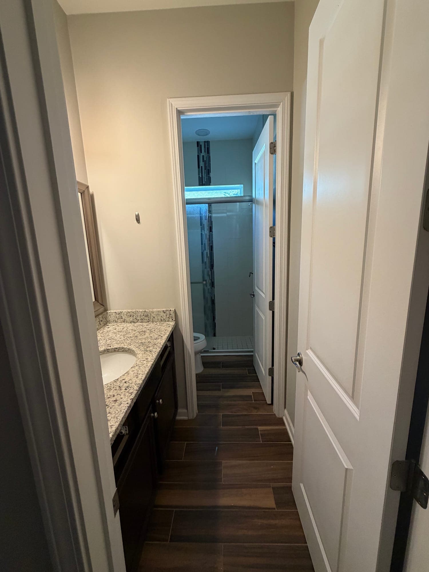 Narrow bathroom before renovation, with a dark wood-look tile floor and the shower closed off behind a separate doorway, in Twenty Mile, Nocatee, Florida